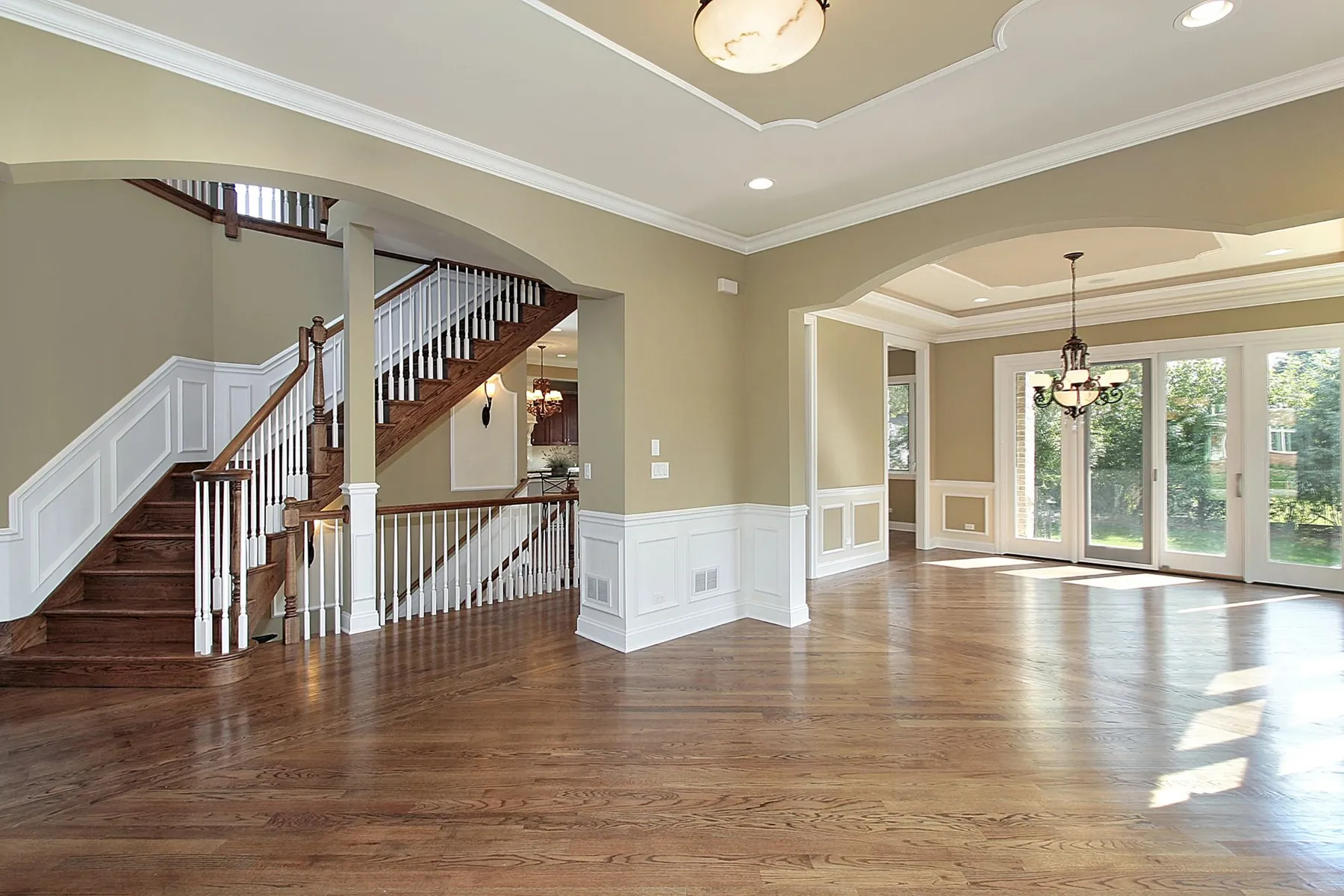 Open plan living area with warm tan walls, white wainscoting, staircase banister and crown molding repainted