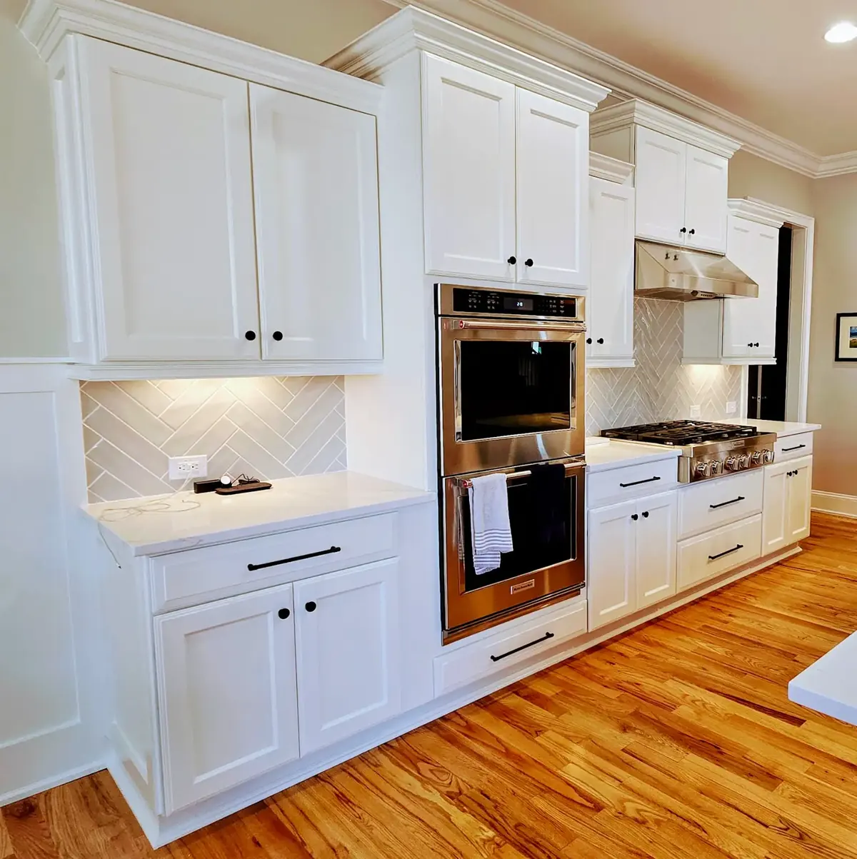 Kitchen with white raised panel cabinets refinished, herringbone backsplash, double wall oven